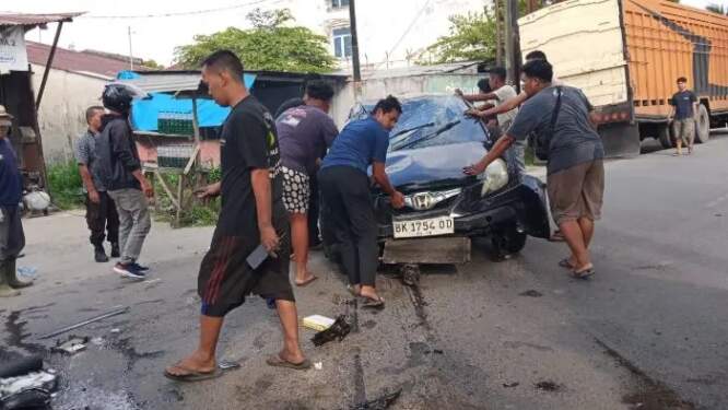 Foto: Warga mengevakuasi mobil yang rusak setelah menabrak tiang listrik di Medan Sunggal.